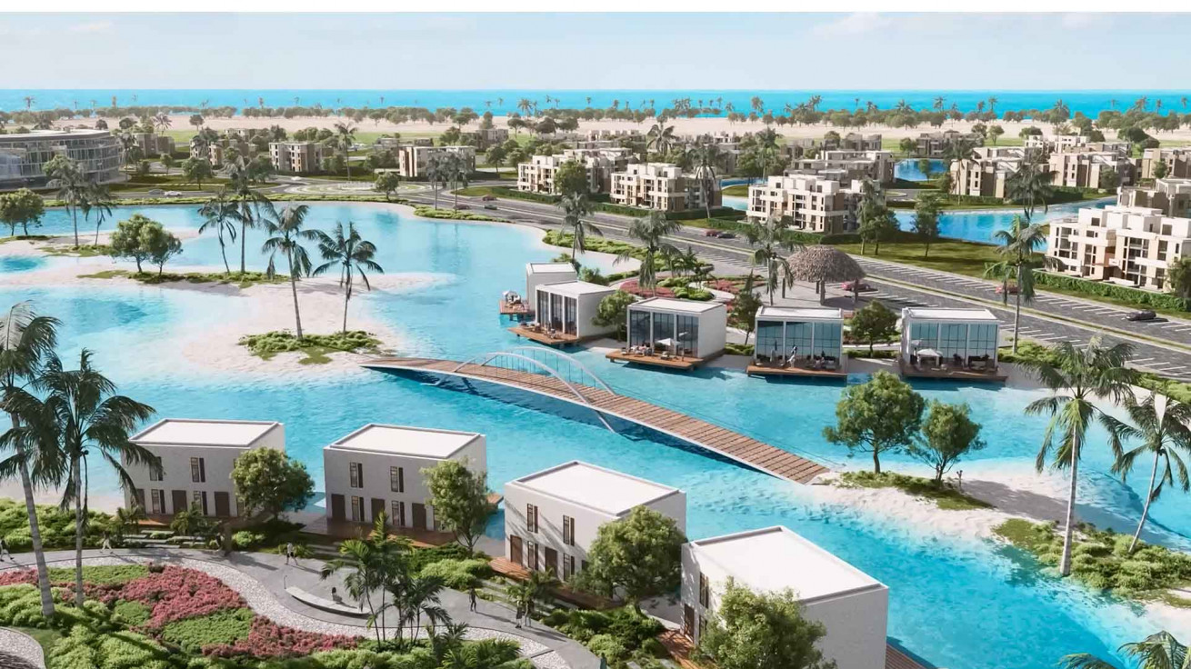 Resort homes along a crystal lagoon with a footbridge and palm islands